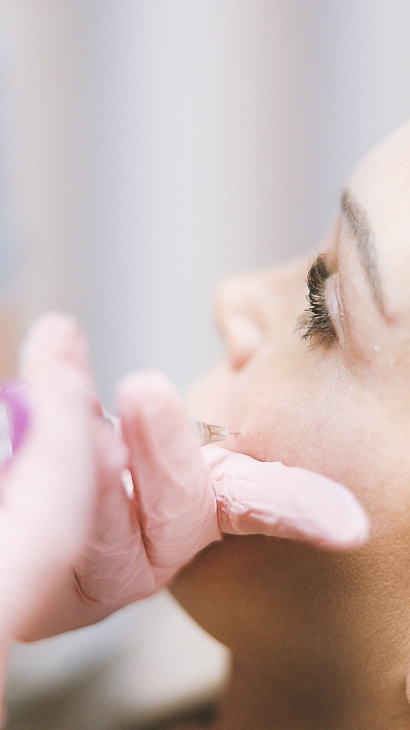 Close-up of a medical professional wearing pink gloves administering a dermal filler injection into a woman's cheek to enhance midface volume and facial contours.