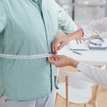 Healthcare professional measuring a patient's waist with a tape measure during a medical weight loss consultation to assess body composition and track progress.