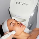 Woman receiving RF microneedling treatment on her cheek using the VirtueRF SmartRF handpiece, with the VirtueRF device visible behind her.