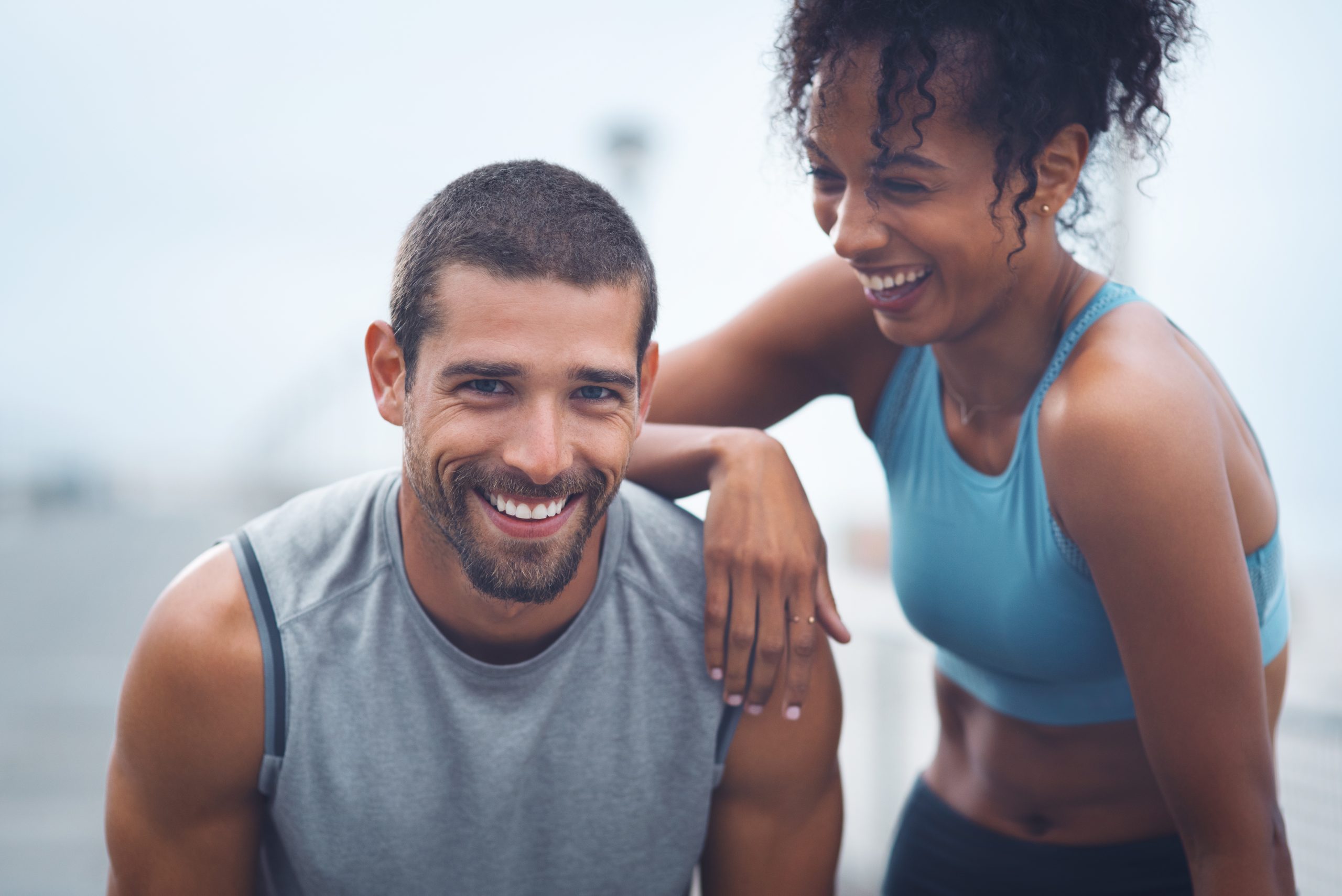 Smiling man in athletic clothing with a woman resting her arm on his shoulder, representing an active lifestyle, confidence, and support for men's health and wellness.