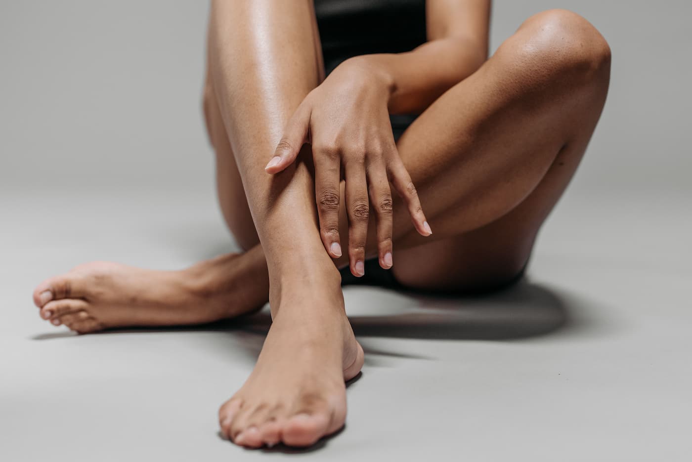 Woman sitting with her legs extended, touching her smooth lower leg, illustrating smooth skin and the benefits of laser hair removal.