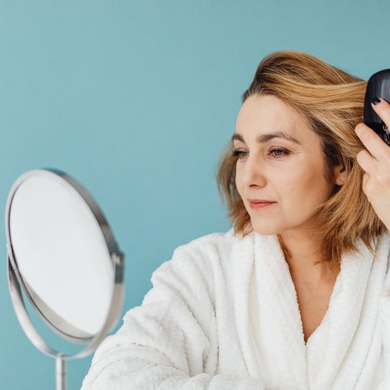 Woman examining her hair in a mirror while gently pulling it back to check her hairline and hair density, illustrating concerns about female hair thinning and hair loss.