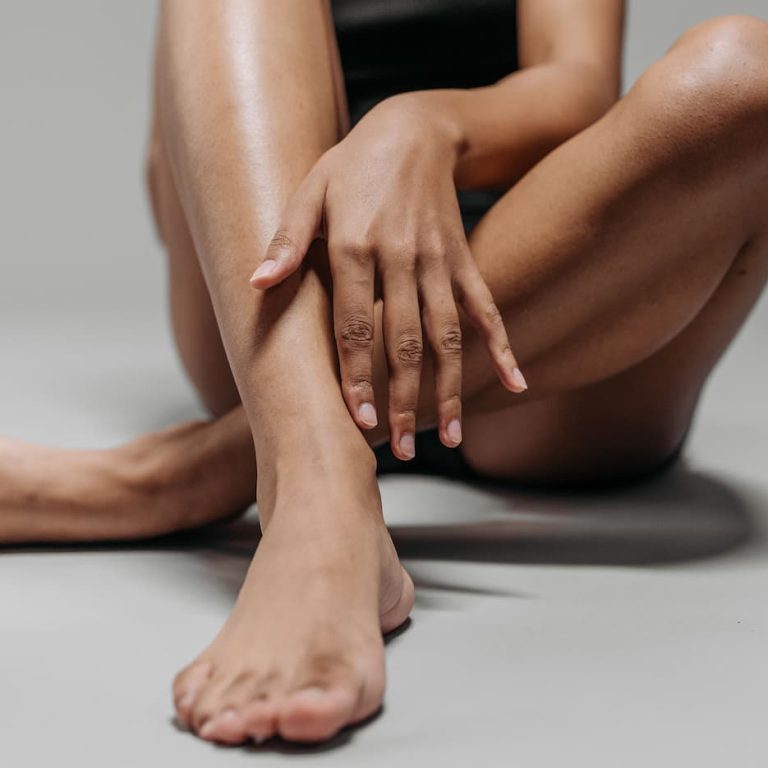 Woman sitting with her legs extended, touching her smooth lower leg, illustrating smooth skin and the benefits of laser hair removal.